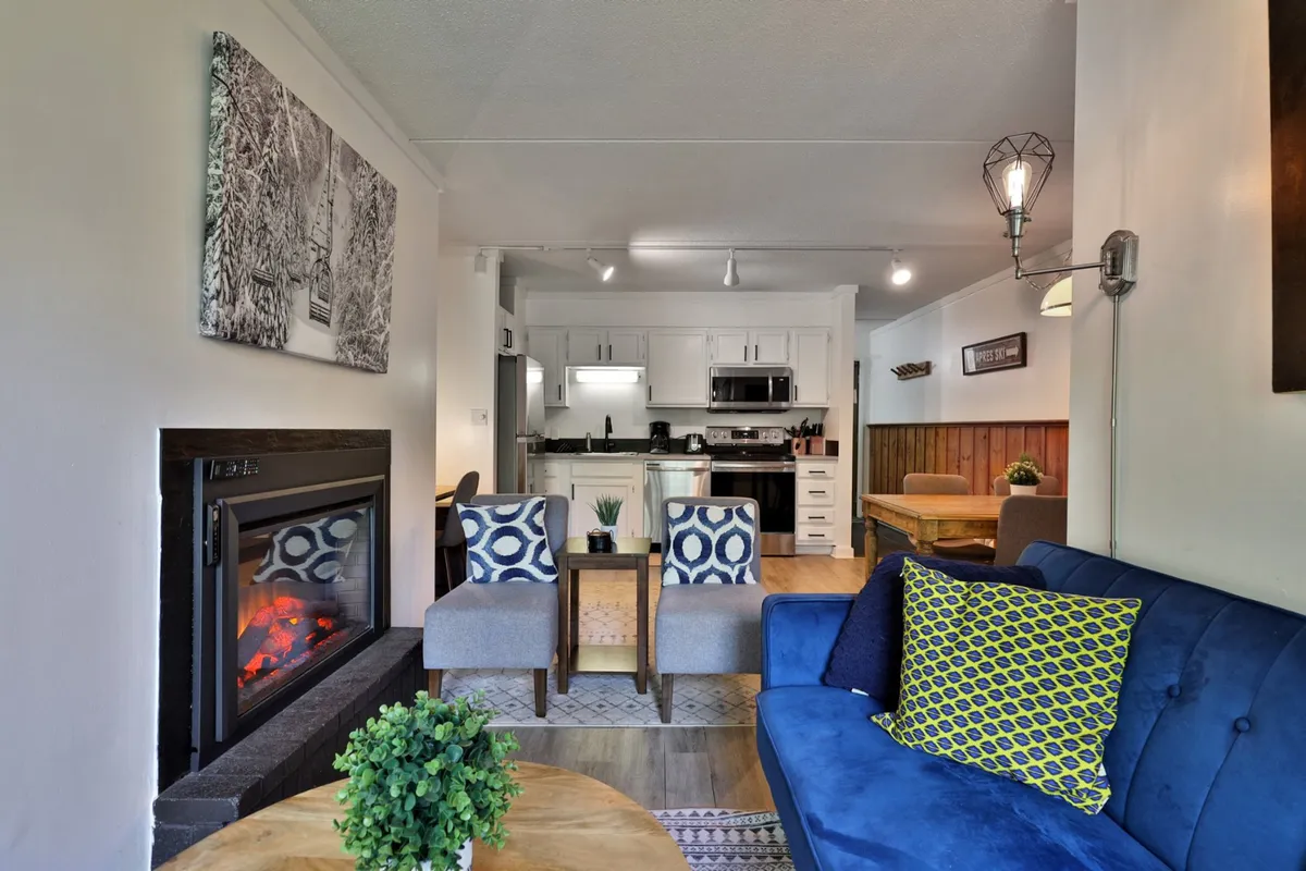 The image showcases a warm, inviting living space with a glowing fireplace, a plush blue sofa, and a dining area perfect for gathering. The ambiance is cozy, ideal for relaxing after a day on the Killington slopes, while the open layout ensures seamless connection between lounging and dining.