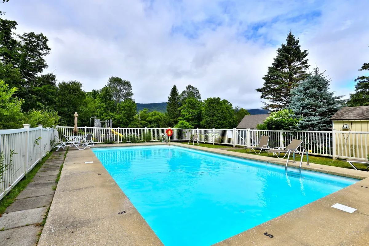 The image showcases a sparkling outdoor swimming pool surrounded by lush greenery and comfortable poolside chairs, with a lifebuoy visible for safety. The area is bathed in sunlight, evoking a leisurely and refreshing summer atmosphere ideal for relaxation, social gatherings, and family fun.