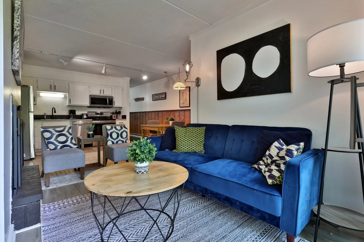 An open-concept space with a blue sofa, round wooden coffee table, and tasteful wall art, with the dining area visible in the background. The room is styled for both relaxation and entertaining, providing a welcoming spot to continue the evening indoors.
