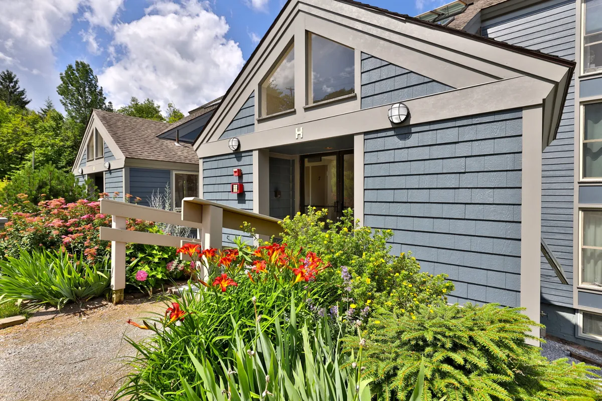 A cheerful exterior view of the condo building, featuring vibrant flower beds, inviting architectural details, and the front entrance. The lush landscaping and sunny ambiance create a welcoming atmosphere ideal for families arriving for a getaway.