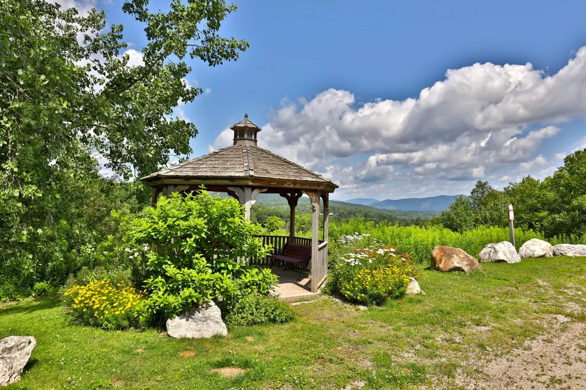 A scenic exterior shot featuring a gazebo surrounded by flowers and a stunning mountain view in the background. The peaceful mood suggests relaxation and opportunities for kids and families to explore and enjoy nature.
